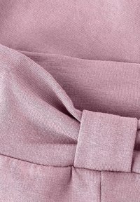 Detailný záber na zloženú mäkkú ružovú pleteninu s viditeľným pásom a detailom nabranej stehovania.