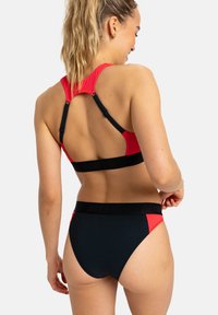 Röd och svart bikinitopp med racerback-design, justerbara axelremmar och logoband nederst. Slät och elastisk material.