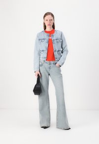 Τζάκετ τζην σε ανοιχτό μπλε, με δύο τσέπες στο στήθος και στρογγυλή κολάρα. Κόκκινη μπλούζα από κάτω, σε συνδυασμό με ανοιχτού μπλε καμπάνα τζιν και μαύρη τσάντα.