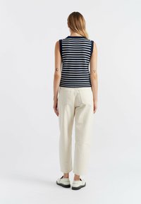 Top senza maniche a righe blu navy e bianche, abbinato a pantaloni color crema. L'outfit presenta un design semplice e una vestibilità comoda, completato da calzature leggere.