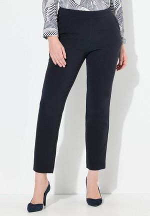 Tmavě modré kalhoty na míru s hladkým povrchem a slim fit. Mají pas bez viditelných zapínání, doplněné o tmavě modré vysoké podpatky.