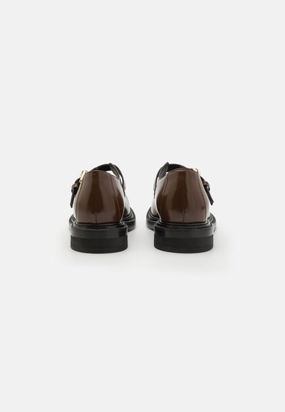 Zapatos de charol marrones con un acabado pulido, suela negra y un acento de hebilla metálica, vistos desde la parte trasera.