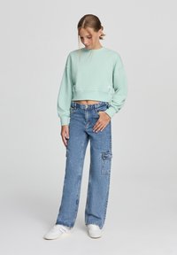 Felpa corta verde menta con collo rotondo e polsini a coste, abbinata a jeans a gamba larga blu chiaro con tasche cargo.