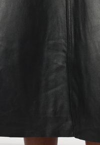 Gonna di pelle nera con una texture liscia, caratterizzata da una cucitura verticale al centro e una leggera lucentezza. I bordi sono rifiniti in modo ordinato.