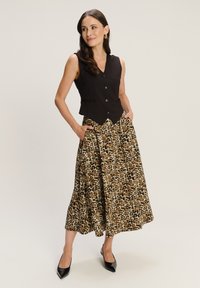 Czarna bezrękawnik z zapięciem na guziki, w połączeniu z midi spódnicą w cętki. Modelka nosi czarne, spiczaste szpilki, które mają warstwowy design.