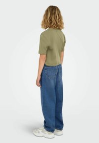 Olivno zeleni kratki crop t-shirt s kratkimi rokavi, v kombinaciji s širšimi, visokim pasom modrim denimom. Obutev so nevtralnih tonov, ki dopolnjujejo obleko.