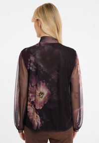 Durchsichtige schwarze Bluse mit langen Ärmeln, die ein florales Muster in Lila- und Rosatönen aufweist, sowie eine weiche, leichte Textur hat.