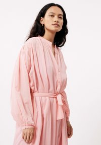 Rosa, langärmliges Kleid aus leichtem Stoff, mit einer durchgehenden Knopfleiste, Raffung und einem gebundenen Taillendetail.