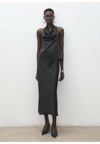 Haut dos nu en satin noir et longue jupe, présentant une texture lisse et une silhouette ajustée, assortis à des talons pointus noirs et des boucles d'oreilles créoles en or.