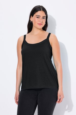 Young woman with straight dark hair wearing a black sleeveless top and black pants, standing against a white background.