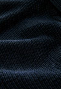 Marineblaues strukturiertes Gewebe mit vertikalem Rippmuster, weichem Plüschgefühl und leichtem Glanz, der Tiefe und Dimension verleiht.