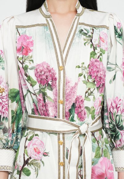 Blomstret kjole med en livlig pink og grøn print, letvægtsstof, guldknapper og et matchende bælte med et fletakcent.