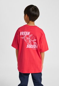 Röd bomullst-shirt med ett stort vitt grafiktryck där det står "FRESH SEASON", med illustrationer av fotbollar och löv på baksidan.