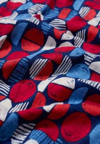 Tela de algodón con un diseño estampado de círculos rojos, azules y blancos, con líneas texturizadas y formas variadas sobre un fondo navy.