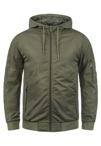 Veste à capuche vert olive avec fermeture éclair sur le devant, poignets élastiques et poche poitrine zippée. Matériau lisse et léger avec un design basique.