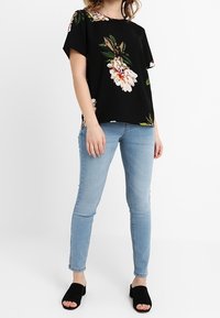 Black floral blouse with short sleeves, featuring large white and pink flowers, paired with light blue skinny jeans and black slide sandals.