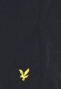 Tessuto blu navy con una superficie liscia presenta un logo di un'aquila gialla ricamato. Design semplice, pochi motivi e nessun hardware visibile.