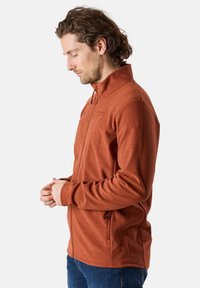 Giacca da uomo con zip di colore arancione bruciato, realizzata in pile testurizzato, con colletto alto, tasche laterali e design aderente.