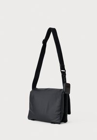 Svart messengerbag i nylon med en glatt tekstur. Justerbar stropp, glidelås lukking, kompakt design, har en liten lomme.