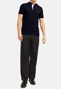 Marineblauwe polo met een henley-halslijn, korte mouwen en witte accenten. Gecombineerd met zwarte geplooide broek en zwarte schoenen.