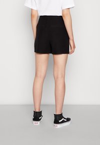 Hochgeschnittene schwarze Shorts mit flachen Gesäßtaschen, aus glattem Stoff, kombiniert mit schwarz-weißen High-Top-Sneakern.