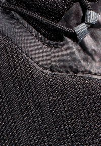 Schwarzer Sportschuh aus strukturiertem Material, Nahaufnahme des Schnürsystems und glatter, strapazierfähiger Materialien. Besitzt dezente Akzente.