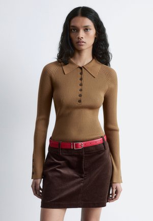 Brown ribbed long-sleeve top with a collared neck and button placket, paired with a brown corduroy skirt and a bright red belt.
