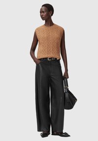 Strik uden ærmer i tan med et struktureret mønster, parret med sorte brede læderbukser og sorte sko, mens der holdes en sort taske.