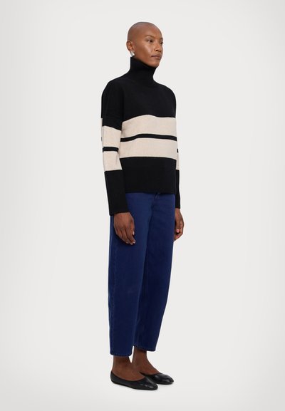 Black and beige striped turtleneck sweater in a thick knit, paired with loose dark blue trousers and black flat shoes.