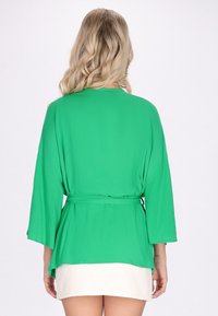 Zeleni zavit kotni top s tremi četrtimi rokavi, izdelan iz lahkega materiala, z vezanjem v pasu in ohlapnim krojem.