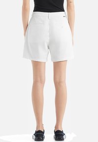 Shorts bianchi in cotone con una vestibilità rilassata, dotati di due tasche posteriori e una cintura pulita, abbinati a scarpe nere.