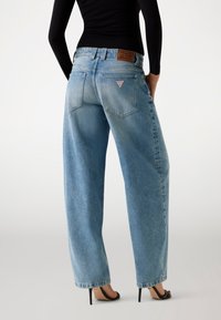 Jeans a gamba larga di colore blu chiaro realizzati in denim, con vita alta, tasca posteriore applicata e dettaglio del logo. Texture liscia con un finish sbiadito.