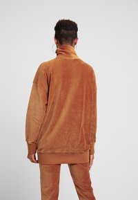 Pull en velours côtelé marron avec un col montant, coupe oversize, épaules tombantes et poignets côtelés, associé à un bas assorti.