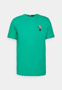 Grøn bomulds T-shirt med rund halsudskæring og korte ærmer, prydet med et lille sort-hvidt grafisk motiv af en karakter på venstre bryst.