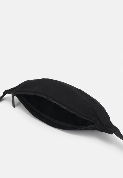 Borsetta di stoffa nera con chiusura a zip, texture morbida, forma leggermente arrotondata e una tracolla corta da un lato. L'interno sembra foderato.