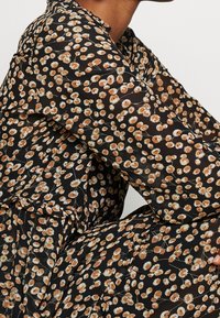 Blusa de tela negra con un estampado floral en blanco y naranja, textura transparente, mangas largas y un corte holgado.