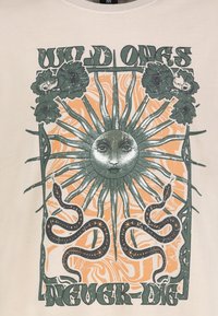 Cremfarbener T-Shirt mit einem grafischen Design, das ein zentrales Sonnenmotiv zeigt, umgeben von Blumen und Schlangen, in erdigen Tönen von Grün und Orange.