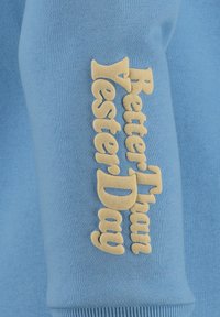Felpa azzurra chiara con lettering beige testurizzato "Better Than Yesterday" sulla manica destra, realizzata in morbido cotone.