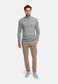 Grå kabelstrikket genser med høy krage, beige bukser og grå joggesko. Enkelt design, glatt tekstur og nøytrale farger.