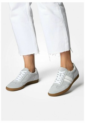 Baskets en daim gris avec des lacets blancs et une bande sur le côté, tige texturée, design bas et semelle en gomme; portées avec des jeans blancs effilochés.