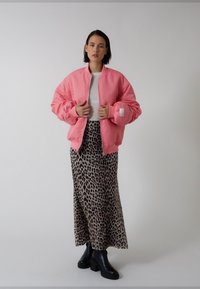 Rozā bomber tipa jaka ar gludu tekstūru, valkāta pāri baltai krekliņai un garai leoparda raksta svārkiem. Melni platformas zābaki papildina tēlu.