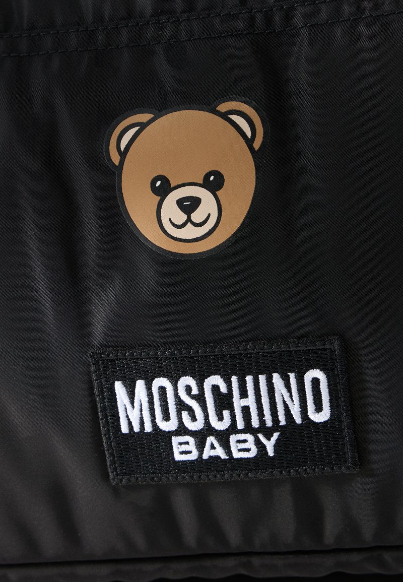 Brown teddy bear face above a black fabric patch with white "MOSCHINO BABY" text on a black background.