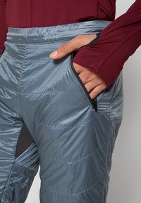 Grå isolerade byxor med en slät yta, utrustade med horisontell sömnad, en ficka med dragkedja på sidan och ett elastiskt midjeband.