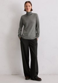 Grauer Rollkragenpullover mit langen Ärmeln, kombiniert mit schwarzen weit geschnittenen Hosen. Das Outfit zeichnet sich durch eine glatte Textur und eine entspannte Passform aus.