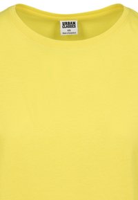 T-shirt en coton jaune avec un col rond, présentant une petite étiquette avec la marque "Urban Classics" et les informations de taille à l'intérieur du col.