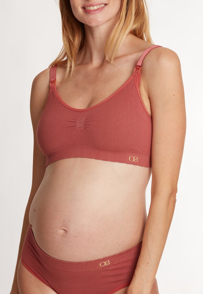 Soutien-gorge de maternité et culottes assorties en tissu côtelé de couleur rose pêche. Caractéristiques : bretelles ajustables, clip latéral pour l'allaitement et accent de logo discret.