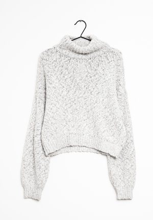 Pull à col roulé en maille épaisse gris clair avec de longues manches ballon suspendu sur un cintre noir sur fond blanc.