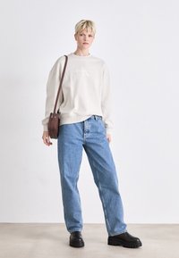 Beige crewneck sweatshirt with Calvin Klein Jeans logo, paired with blue relaxed-fit jeans and black platform boots. Brown crossbody bag included.