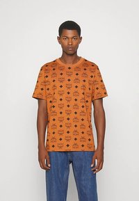 Orange kortärmad t-shirt med ett upprepat svart logomönster. Klassisk rund halsringning och en bekväm passform.