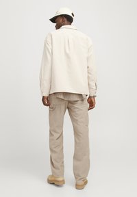 Light beige corduroy jacket with a relaxed fit, paired with matching cargo pants. The outfit includes a cream cap and textured accents.